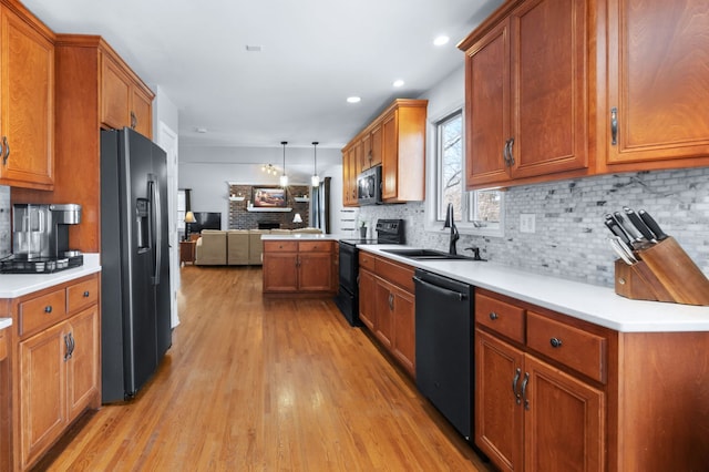 kitchen featuring sink, decorative backsplash, hanging light fixtures, black appliances, and light hardwood / wood-style flooring