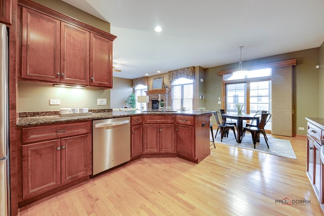 kitchen featuring sink, dark stone countertops, hanging light fixtures, stainless steel dishwasher, and light wood-type flooring