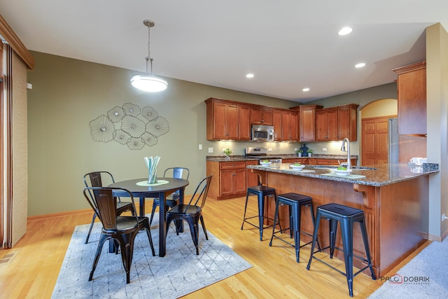 kitchen featuring stainless steel appliances, sink, dark stone countertops, and light hardwood / wood-style flooring