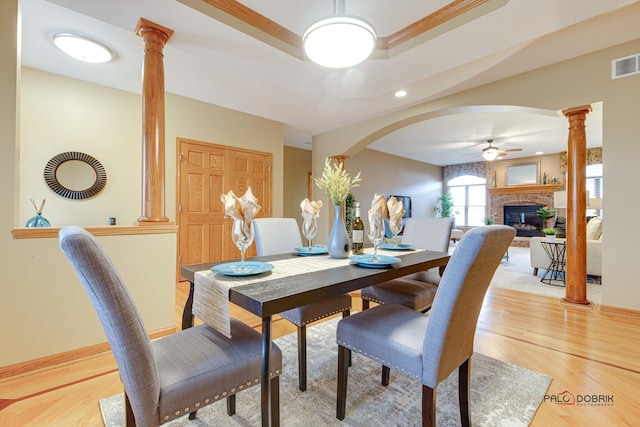 dining space with a brick fireplace, decorative columns, light hardwood / wood-style floors, and ceiling fan