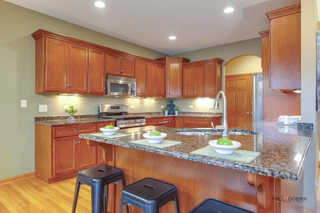 kitchen featuring sink, stainless steel appliances, a kitchen bar, kitchen peninsula, and dark stone counters