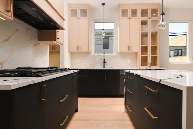 kitchen with stainless steel gas stovetop, sink, hanging light fixtures, custom range hood, and light hardwood / wood-style flooring