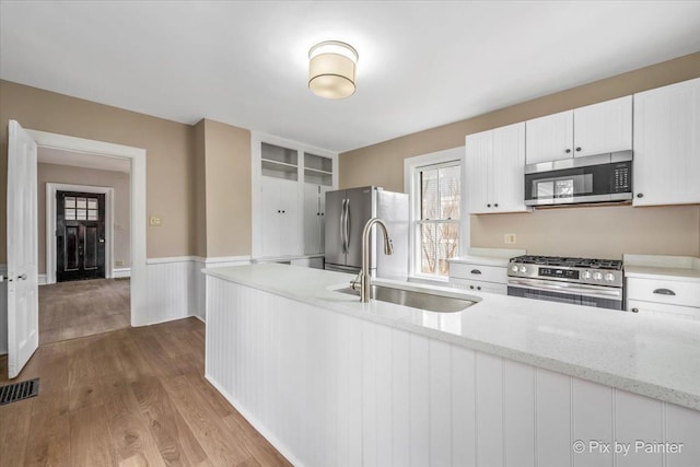 kitchen featuring sink, appliances with stainless steel finishes, white cabinetry, light stone counters, and light hardwood / wood-style floors