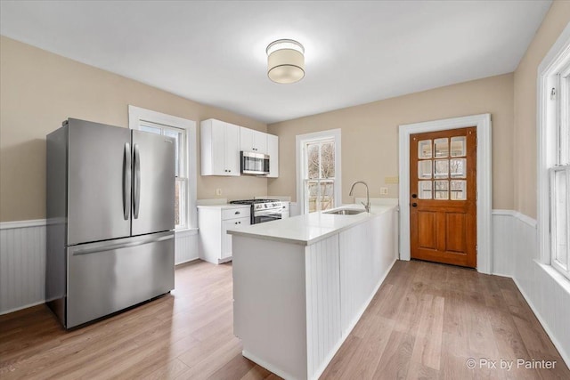 kitchen with sink, white cabinetry, light hardwood / wood-style flooring, appliances with stainless steel finishes, and kitchen peninsula