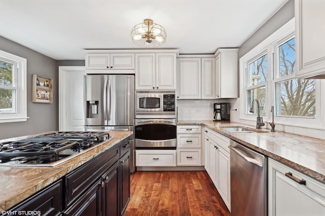 kitchen with a sink, backsplash, wood finished floors, white cabinetry, and stainless steel appliances