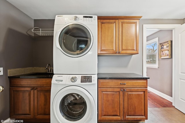 laundry area with baseboards, stacked washer and clothes dryer, light tile patterned flooring, cabinet space, and a sink