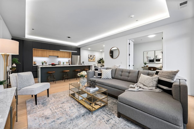 living room featuring a tray ceiling, sink, and light hardwood / wood-style flooring