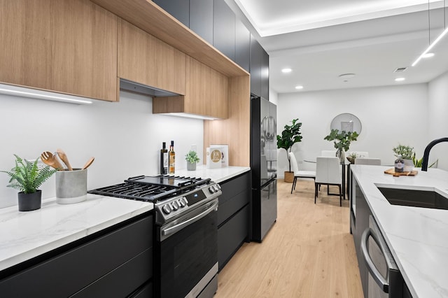 kitchen with light stone counters, sink, gas range, and black fridge