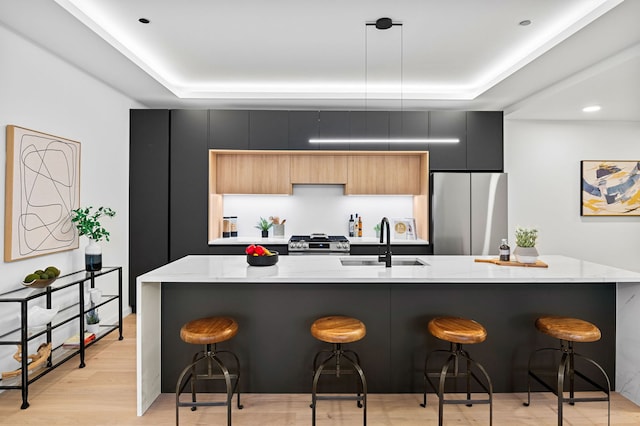 kitchen with sink, a breakfast bar area, stainless steel fridge, hanging light fixtures, and range