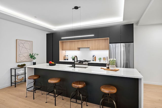 kitchen featuring pendant lighting, a tray ceiling, stainless steel fridge, and a center island with sink