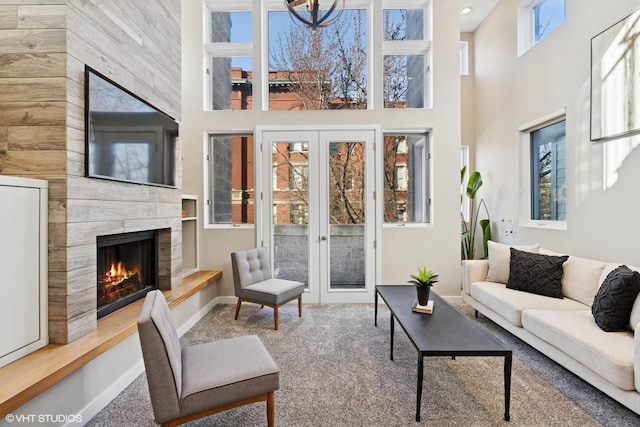 carpeted living room with baseboards, a high ceiling, a high end fireplace, and french doors