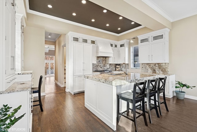 kitchen with an island with sink, a breakfast bar area, premium range hood, white cabinetry, and a sink