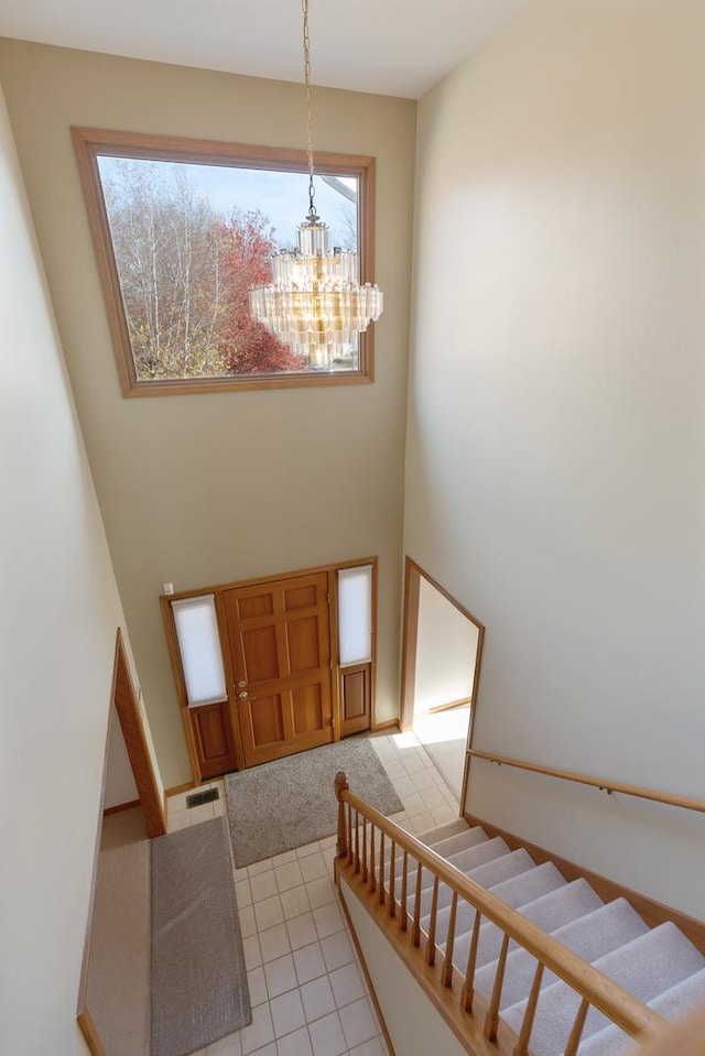 entrance foyer featuring visible vents, stairway, a high ceiling, a notable chandelier, and light tile patterned flooring