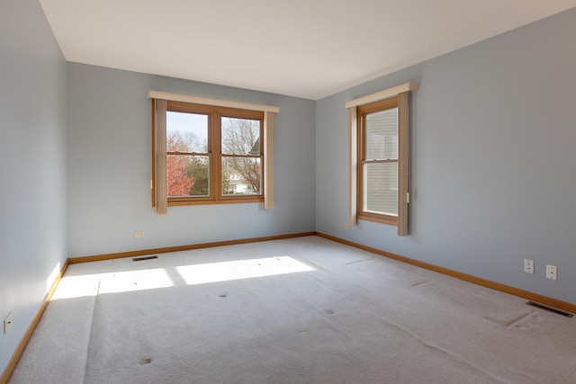 spare room featuring light colored carpet, visible vents, and baseboards