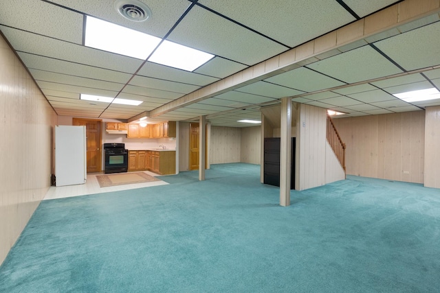 finished below grade area with a paneled ceiling, light colored carpet, visible vents, freestanding refrigerator, and wooden walls