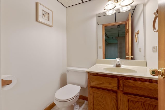 bathroom featuring baseboards, a drop ceiling, vanity, and toilet