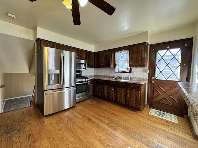 kitchen with dark brown cabinetry, stainless steel appliances, a sink, light wood-style floors, and light countertops