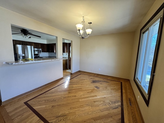 empty room with light wood-style floors, baseboards, visible vents, and ceiling fan with notable chandelier