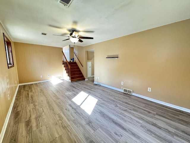 empty room featuring light wood-style floors, visible vents, ceiling fan, and stairway