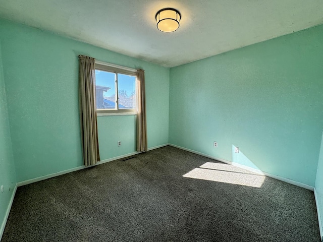 spare room with dark colored carpet, visible vents, and baseboards