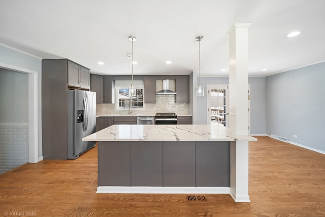 kitchen with light wood finished floors, wall chimney exhaust hood, appliances with stainless steel finishes, decorative light fixtures, and gray cabinets