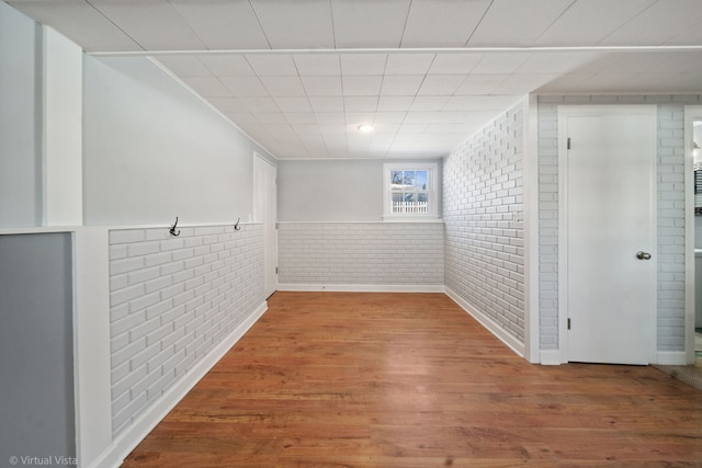 interior space with a wainscoted wall, brick wall, and wood finished floors