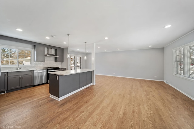 kitchen with decorative light fixtures, appliances with stainless steel finishes, a kitchen island, a sink, and wall chimney exhaust hood