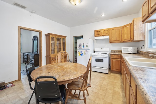 kitchen featuring light floors, visible vents, a sink, white appliances, and under cabinet range hood