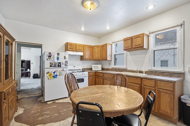 kitchen featuring white appliances, dark countertops, brown cabinets, a sink, and recessed lighting