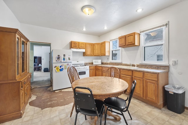 kitchen featuring recessed lighting, brown cabinetry, a sink, white appliances, and under cabinet range hood