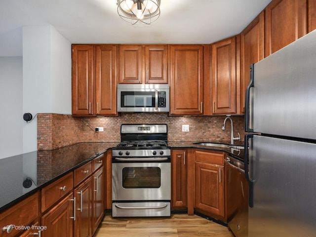 kitchen featuring brown cabinets, dark stone countertops, stainless steel appliances, and a sink