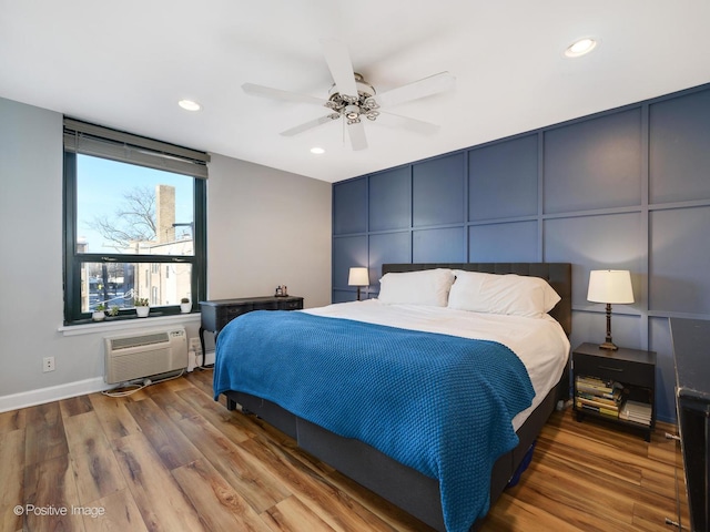 bedroom featuring a wall unit AC, recessed lighting, a decorative wall, ceiling fan, and wood finished floors