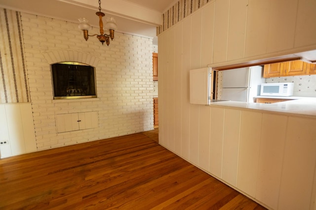 interior space with dark hardwood / wood-style flooring, a notable chandelier, and brick wall