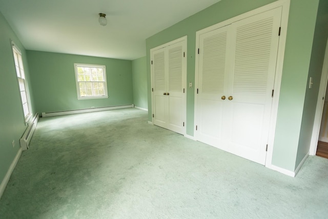 unfurnished bedroom with light colored carpet, two closets, and a baseboard heating unit