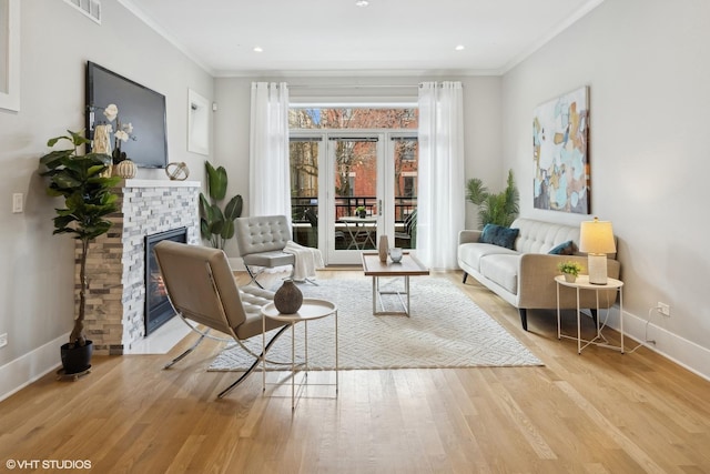 living area with visible vents, ornamental molding, a glass covered fireplace, wood finished floors, and baseboards