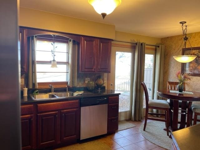 kitchen featuring dark countertops, light tile patterned flooring, dishwasher, and a sink