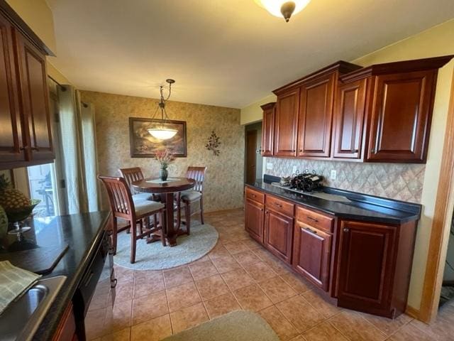 kitchen with light tile patterned floors, hanging light fixtures, decorative backsplash, dark countertops, and wallpapered walls