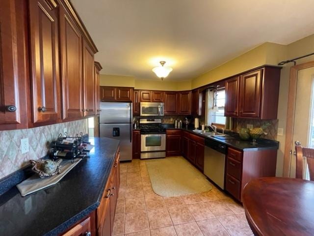 kitchen featuring light tile patterned floors, tasteful backsplash, dark countertops, appliances with stainless steel finishes, and a sink