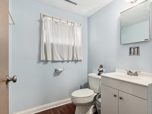 half bath with vanity, wood finished floors, visible vents, baseboards, and toilet