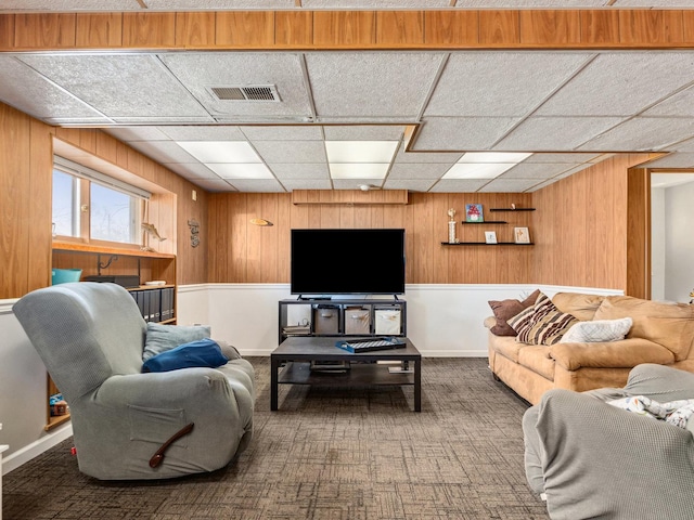 living area with wooden walls, carpet flooring, visible vents, and a drop ceiling