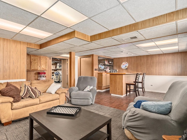 living area featuring visible vents, dark wood-style floors, a bar, wood walls, and a paneled ceiling