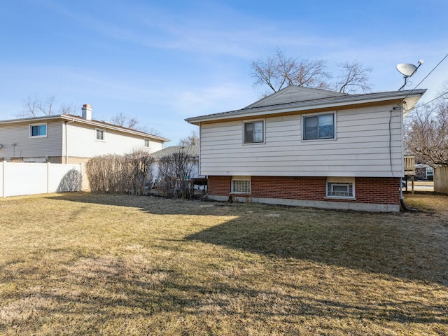 back of house with brick siding, a lawn, and fence