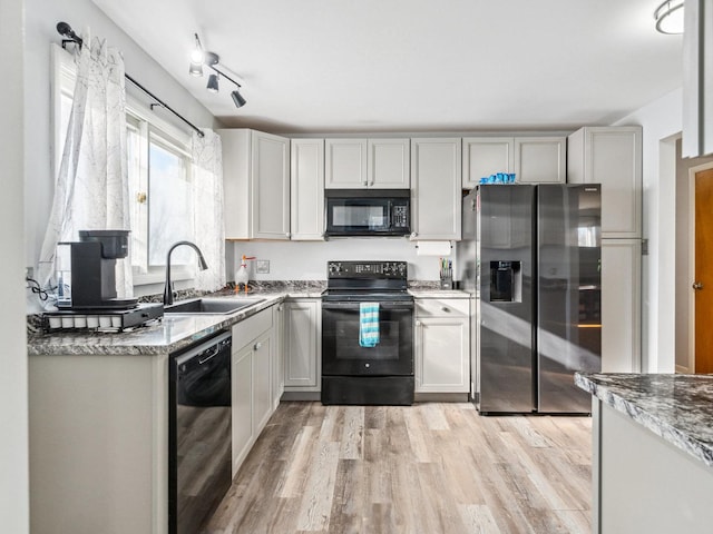 kitchen featuring track lighting, light wood-type flooring, light stone counters, black appliances, and a sink