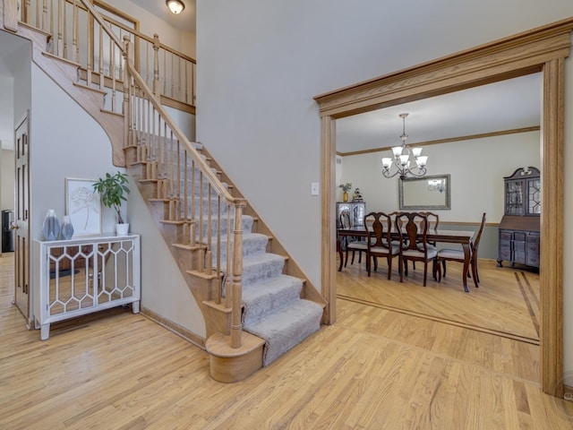 staircase with an inviting chandelier, wood-type flooring, and ornamental molding