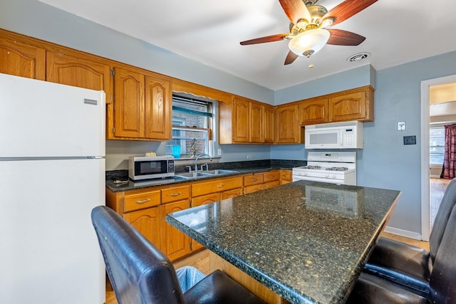 kitchen featuring sink, white appliances, a center island, a kitchen breakfast bar, and ceiling fan