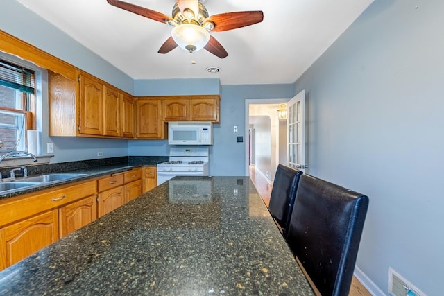 kitchen featuring ceiling fan, sink, dark stone countertops, and white appliances