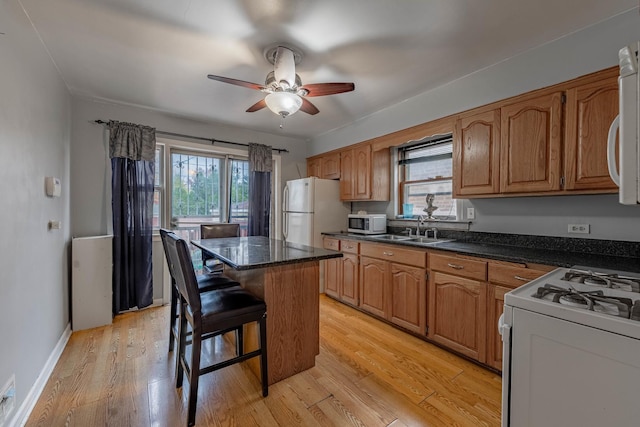 kitchen with sink, white appliances, a kitchen breakfast bar, a center island, and light hardwood / wood-style floors