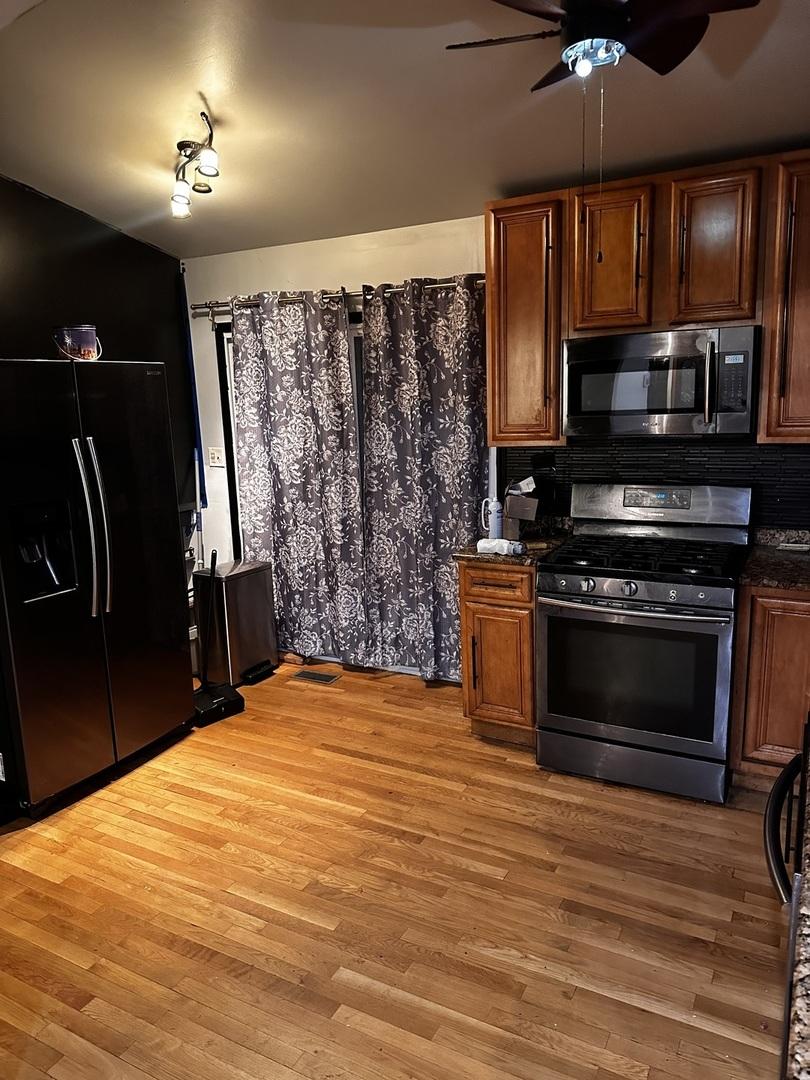 1422 Memorial Dr, Calumet City, IL 60409 - kitchen with gas stove, black refrigerator with ice dispenser, a ceiling fan, and dark countertops