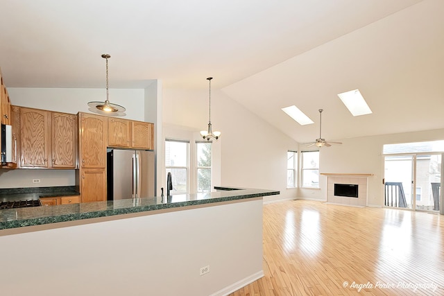 kitchen featuring high vaulted ceiling, pendant lighting, light wood finished floors, freestanding refrigerator, and a skylight