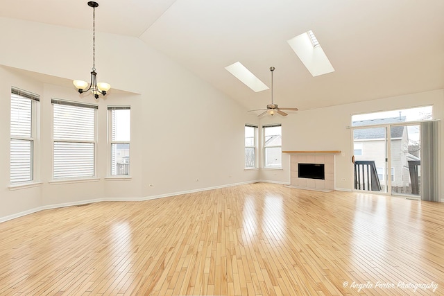 unfurnished living room with high vaulted ceiling, a tile fireplace, a skylight, light wood finished floors, and baseboards
